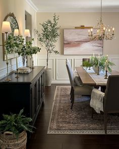 a dining room table and chairs in front of a painting on the wall with candles