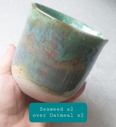 a hand holding a green and white cup with blue lettering on it that says seaweed x2 over oatmeal xx?