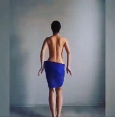 a man with no shirt standing in front of a white wall wearing a blue towel