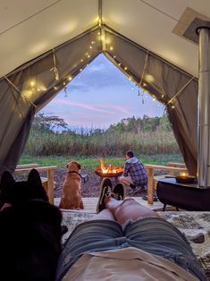 a man and his dog sitting in front of a campfire with their feet on the ground