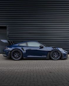 a dark blue sports car parked in front of a garage door with its doors open