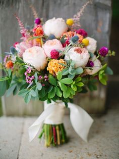 a bouquet of flowers in a vase on a table with greenery and other things