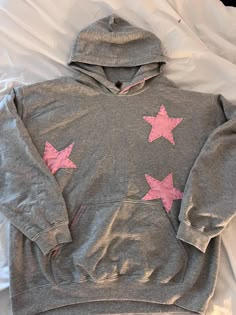 a gray sweatshirt with pink stars on it laying on top of a white sheeted bed