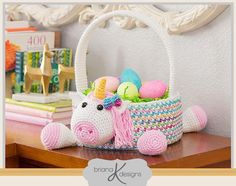 a crocheted unicorn toy sitting on top of a wooden table next to a basket filled with eggs