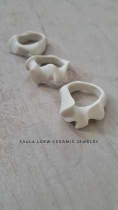 two white ceramic rings sitting on top of a wooden table with the words paula low ceramics jewelry