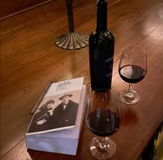 a bottle of wine and two glasses on a table with an old photo next to it