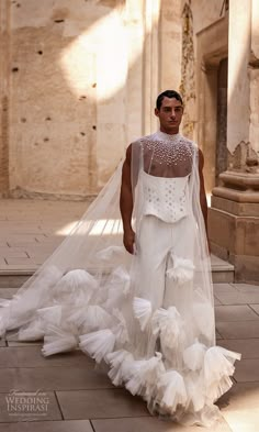 a man in a white wedding gown and veil walks down the street with his back to the camera