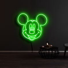 a mickey mouse neon sign on the wall next to a table with a lit candle