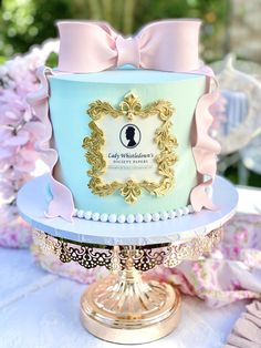 a blue and gold cake with a pink bow on it's top sitting on a table