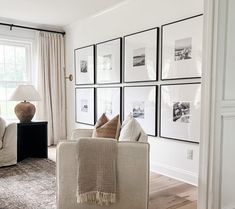 a living room filled with white furniture and pictures on the wall above it's windows