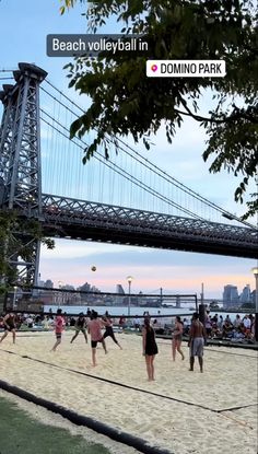 people playing volleyball on the beach in front of a bridge