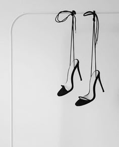 two pairs of high heeled shoes hanging from a rope in front of a white wall