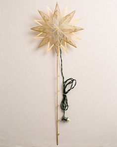 a gold star shaped object with string attached to it's side against a white wall