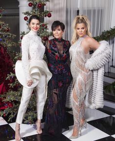 three women standing next to each other in front of a christmas tree