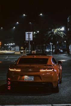 an orange sports car is parked on the side of the road at night with street lights in the background