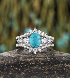 a turquoise stone and diamond ring sitting on top of a rock