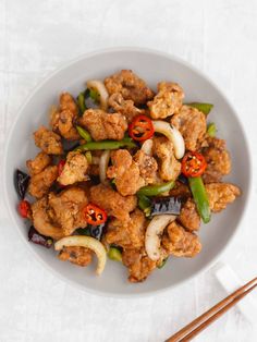 a white bowl filled with meat and vegetables next to chopsticks on a table