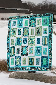 a blue and green quilt sitting on top of snow covered ground