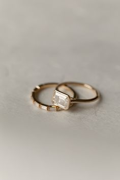 two gold wedding rings with an emerald stone on the top and one diamond in the middle