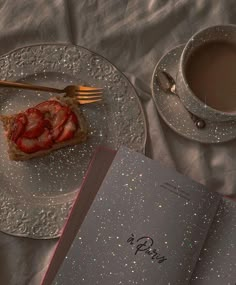 there is a piece of cake on the plate next to a cup of coffee and an open book