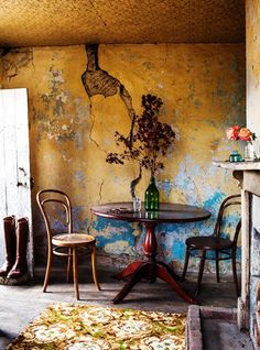 a table and two chairs in front of a yellow wall with peeling paint on it