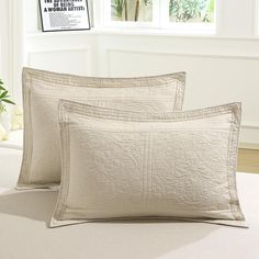 two white pillows sitting on top of a bed next to a vase with flowers in it