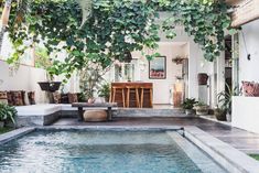 an outdoor living area with a pool and patio furniture in the foreground, surrounded by greenery