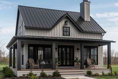 a small house with a porch and covered in black metal roofing, sitting on the grass