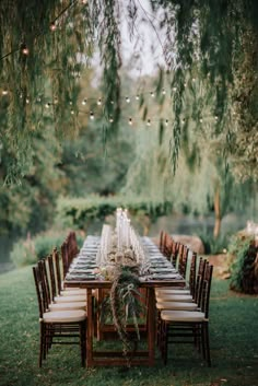 an outdoor dinner table set up with white linens and greenery, surrounded by hanging lights