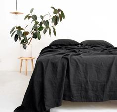 a bed covered in black linen next to a potted plant