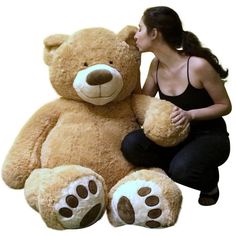 a woman sitting next to a giant teddy bear with paws on it's face