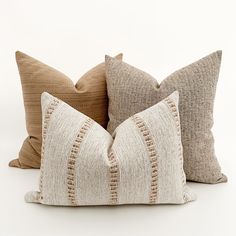 three decorative pillows sitting side by side on top of each other, one in beige and the other in brown