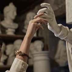 two hands reaching out to each other in front of shelves with white vases on them