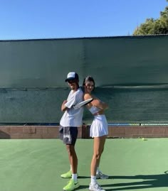 two people standing on a tennis court holding racquets and posing for the camera