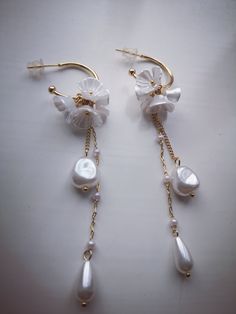 two pairs of dangling earrings with pearls and gold chains on a white surface, the one in the foreground