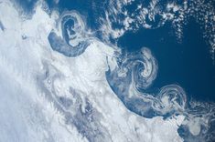 an aerial view of the earth with clouds and blue water in the foreground, taken from space