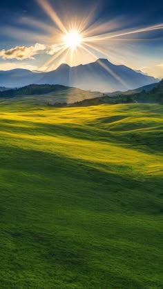 the sun shines brightly over an open field with mountains in the background and green grass