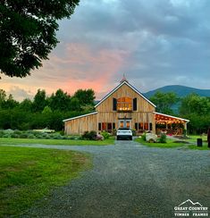 a car is parked in front of a large barn with mountains in the background at sunset