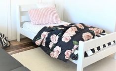 a white bed with pink and black flowers on it, next to a zebra print rug