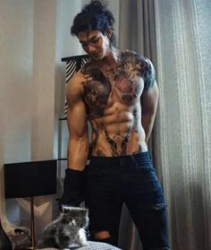 a man with tattoos standing next to a cat