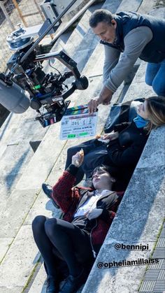 a man sitting on the ground next to a woman holding a sign and pointing at something