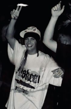 a man in a white shirt and hat holding up a cell phone while standing next to another person