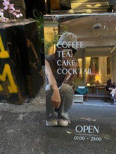 a man sitting on the ground next to a sign that says coffee cake and cocktail