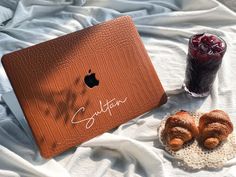 an apple laptop sitting on top of a bed next to two croissants