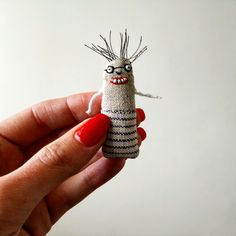 a hand holding a tiny doll with glasses on it's head and red nails