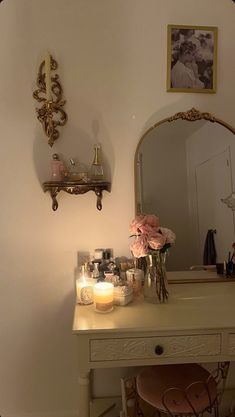 a vanity with flowers and candles on it next to a wall mounted mirror in a room