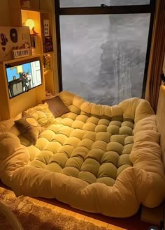 a bed made to look like a couch in front of a window with the tv on