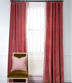 a green chair sitting in front of a window with red curtains on the windowsill