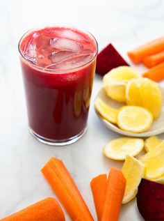 carrots, beets and lemon slices are on the table next to a glass of juice