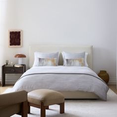 a white bed with two pillows on top of it next to a chair and ottoman